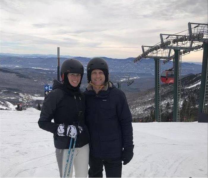 Two People smiling in ski suits ontop of a mountain